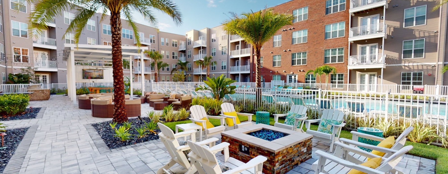 a patio with Adirondeck chairs around a fire pit in a courtyard with palm trees
