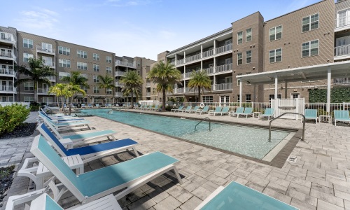 resort style pool with seating palm trees and a building behind it